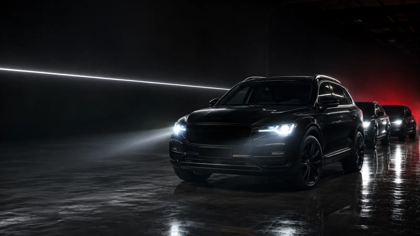Black SUV with headlights on in a dark showroom, a line-up of cars behind it